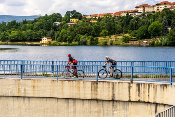 Deutschland © MountainloversTVE Zwei Radfahrer auf einer Brücke über einem See, Häuser im Hintergrund