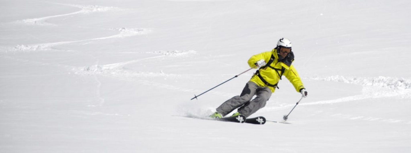 Skifahrer in gelber Jacke fährt auf schneebedecktem Hang