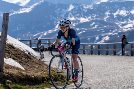 Fietsster in racekleding fietst op bergweg met besneeuwde bergen op achtergrond