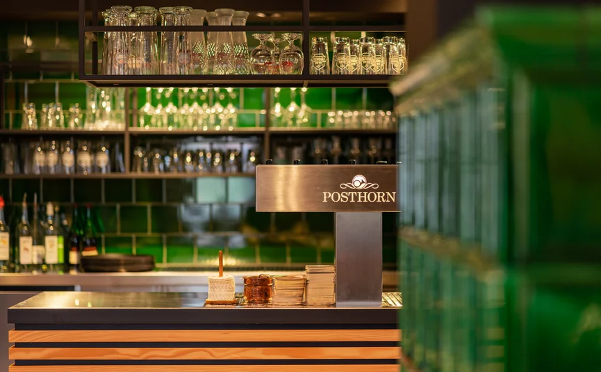 Posthorn Hotel-Ristorante Bar con piastrelle verdi, bicchieri e bottiglie dietro un bancone con insegna Posthorn