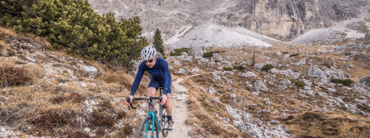 Gravel Adventure Week Cyclist riding on mountain trail with rocky peak behind