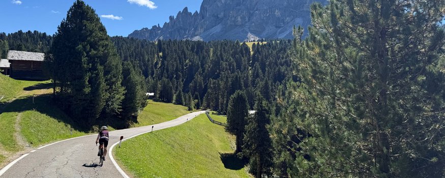 Hotel Ostaria Posta **** © Ueberall GmbH Ciclista su strada di campagna con montagne e foresta sotto cielo azzurro