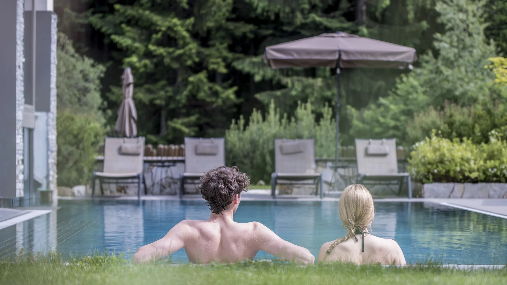 Couple relaxing in a pool with lounge chairs and umbrella in background
