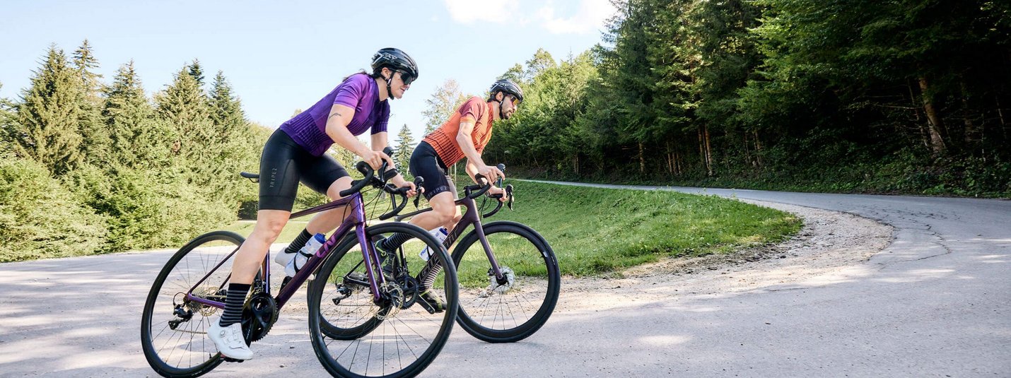 Rennrad Urlaub in Bayern © Tobias Köhler Zwei Radfahrer auf der Straße in einer bergigen Waldlandschaft.