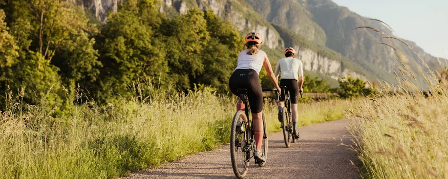 Golden autumn on the road bike in Tramin Two cyclists riding on a path with mountains in the background