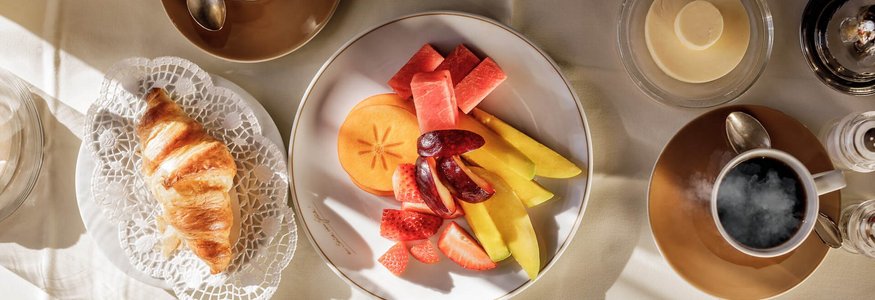 Frühstückstisch mit Croissant, Obstplatte und Kaffee bei Tageslicht