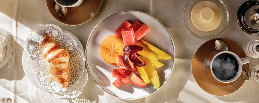 Frühstückstisch mit Croissant, Obstplatte und Kaffee bei Tageslicht