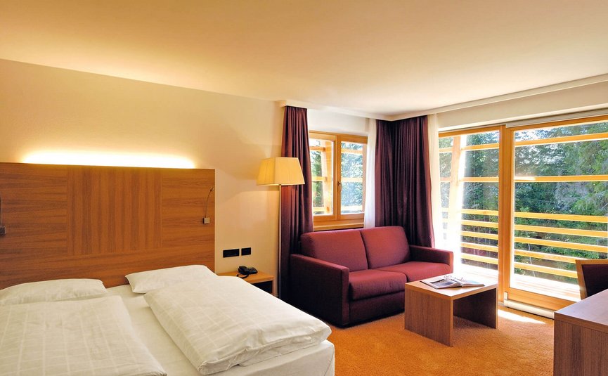 Camera luminosa con letto matrimoniale, divano viola e grandi finestre