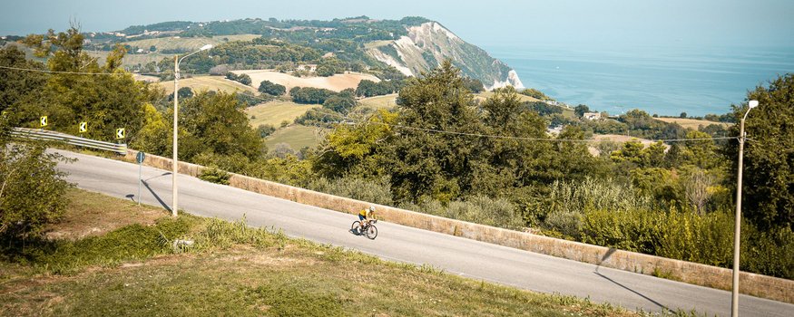 Cyclist on road with hills and sea in the background on clear day