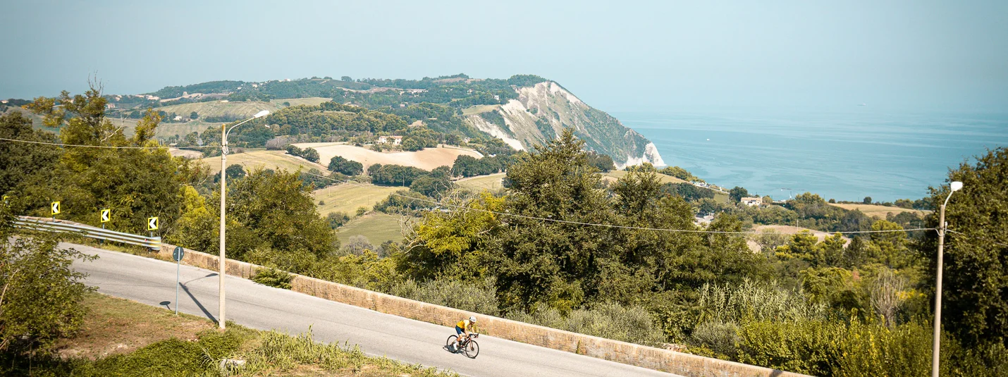 WOW, was für eine Aussicht © Alain Rumpf Radfahrer auf Straße mit Hügeln und Meer im Hintergrund bei klarem Himmel