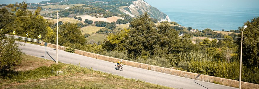 Cyclist on road with hills and sea in the background on clear day
