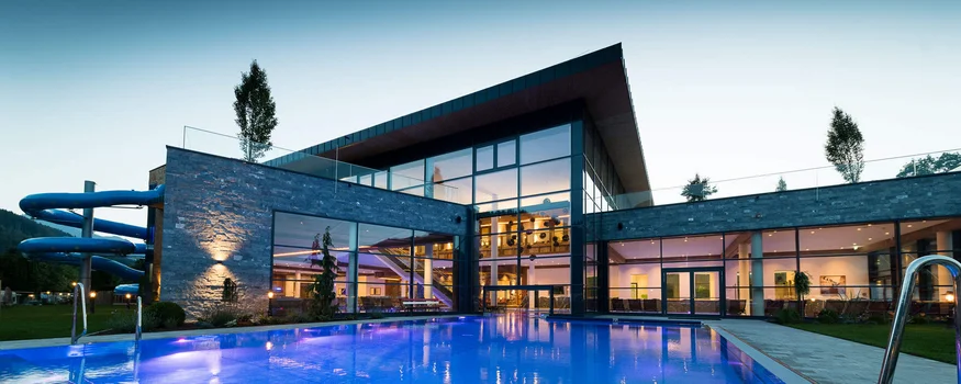 Modern gebouw met verlicht zwembad en waterglijbaan bij schemering