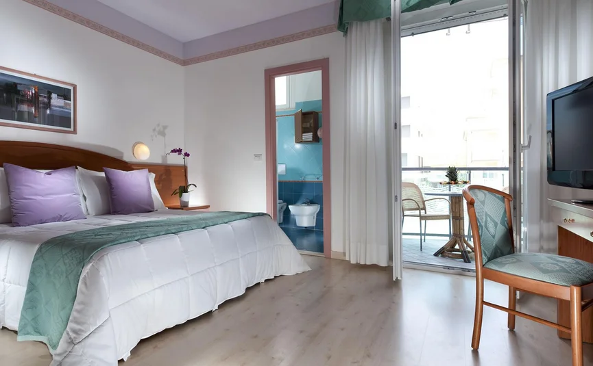 Lichte hotelkamer met tweepersoonsbed, badkamer en balkon met tafel en stoelen