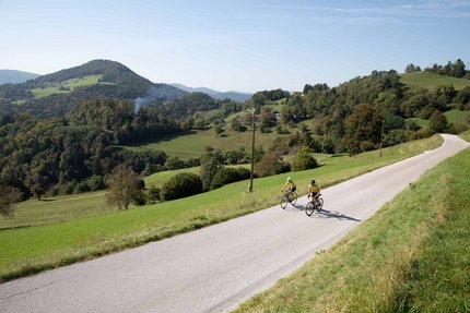 Due ciclisti su strada di campagna con colline verdi sullo sfondo