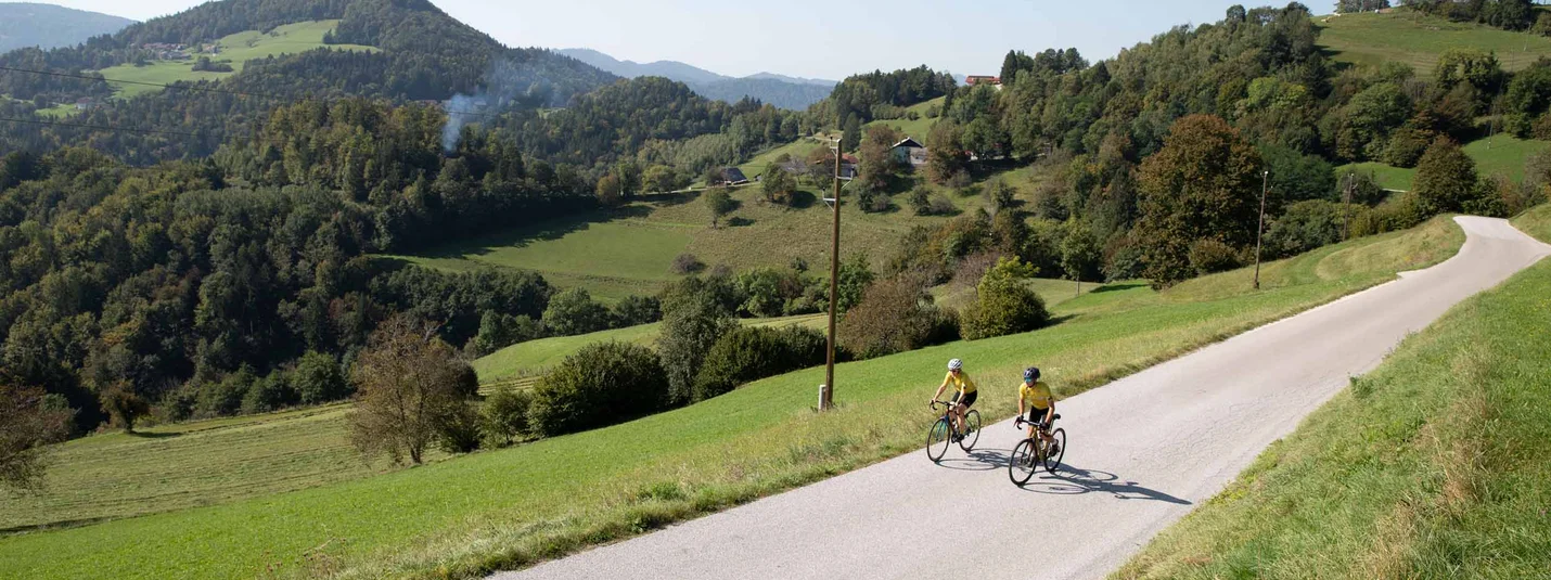 Veliki Dolomiti road bike tour © Kaja Ribezl Two cyclists riding on a country road with green hills in background