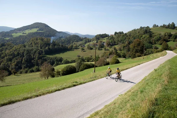 Slowenien © Kaja Ribezl Zwei Radfahrer auf Landstraße mit grüner Hügellandschaft im Hintergrund