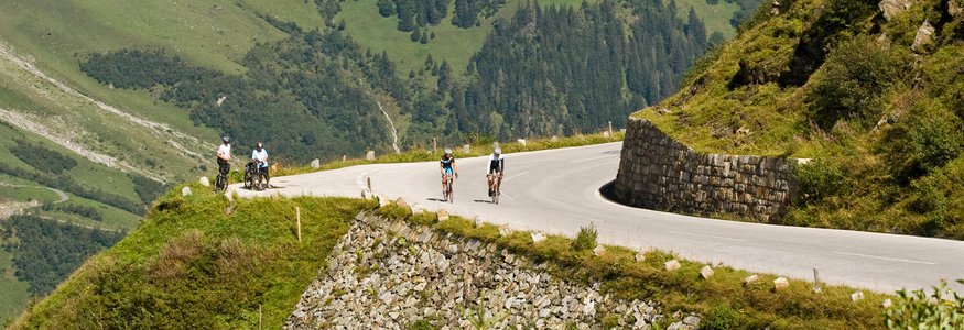 Ciclisti su strada di montagna curva con alberi e nuvole intorno