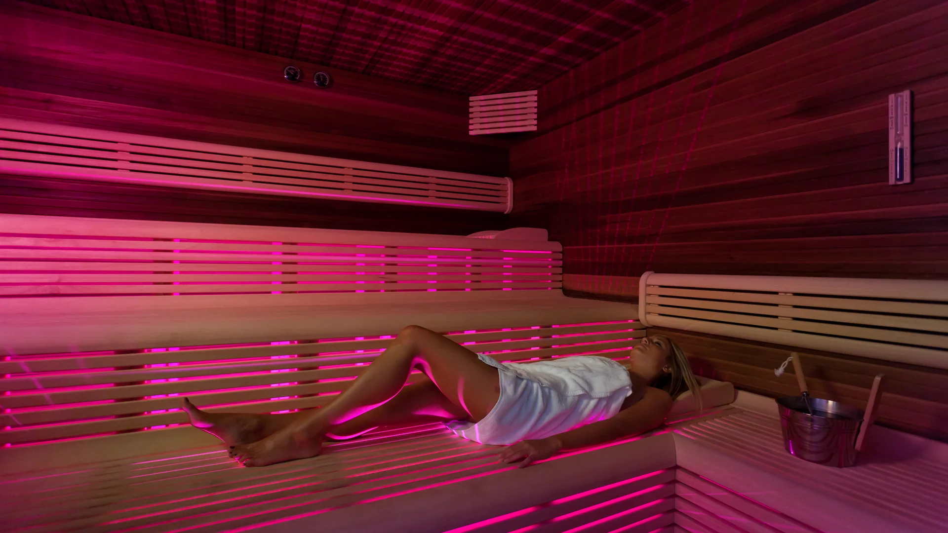 Woman relaxing in modern sauna with pink lighting