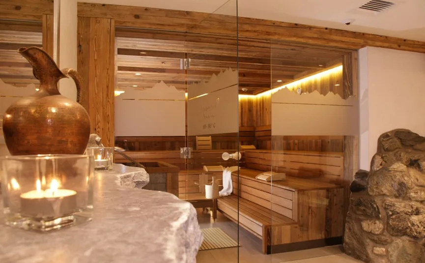 Holzsauna mit Glastür, Kerzen und Steinwand im Wellnessbereich