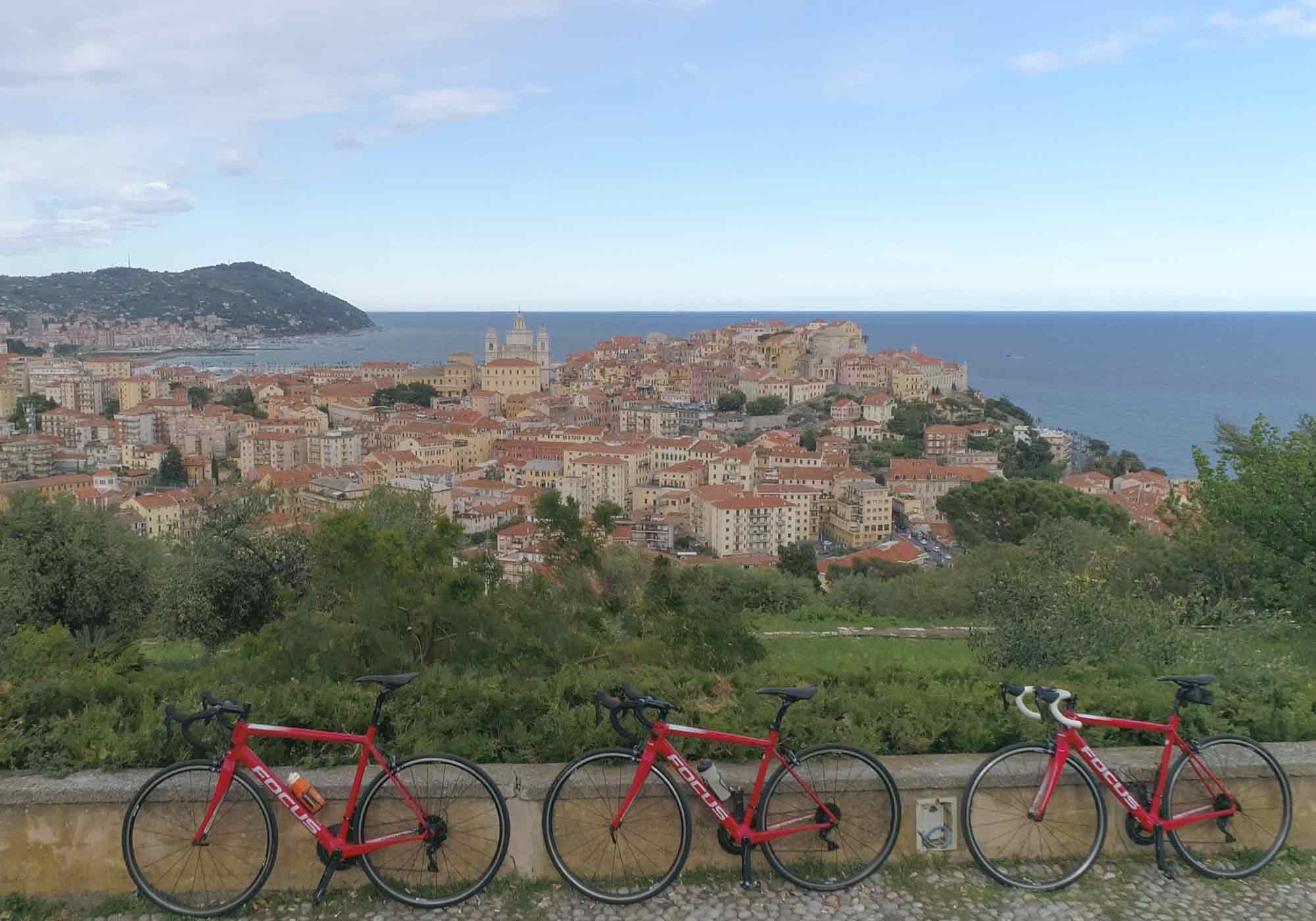 Drie rode racefietsen met uitzicht op een kuststad onder een blauwe lucht