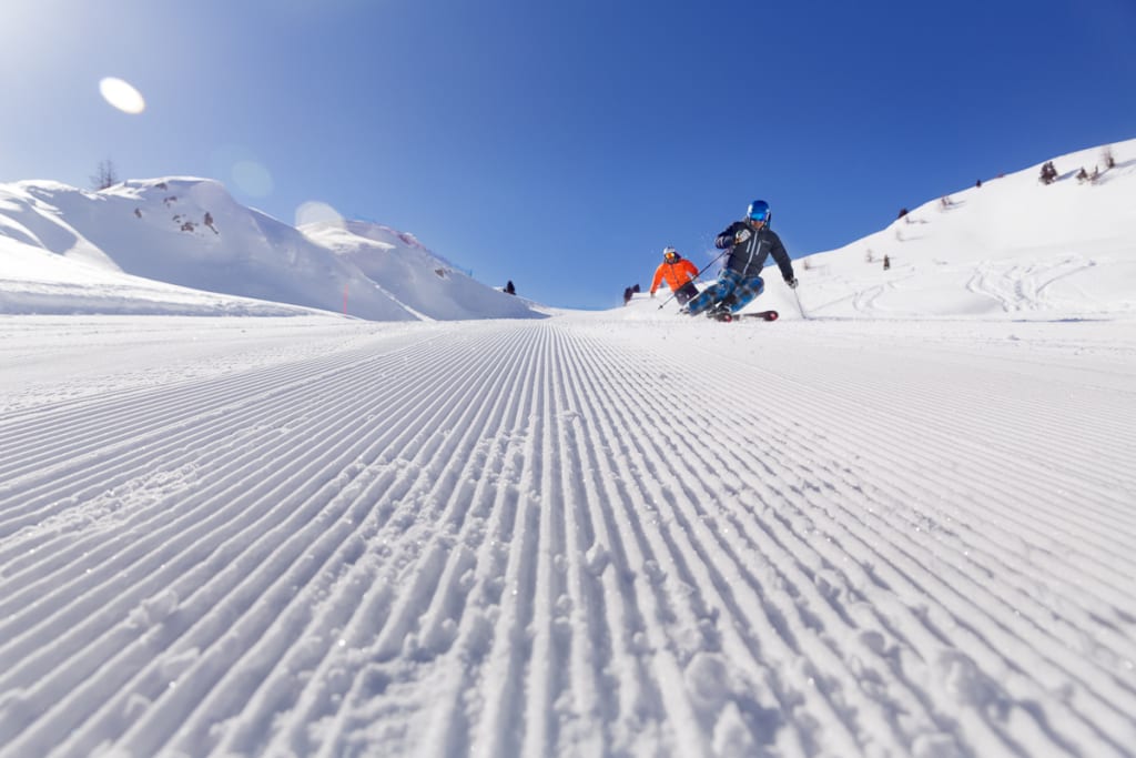 Zwei Skifahrer fahren auf einer frisch präparierten Piste im sonnigen Winter