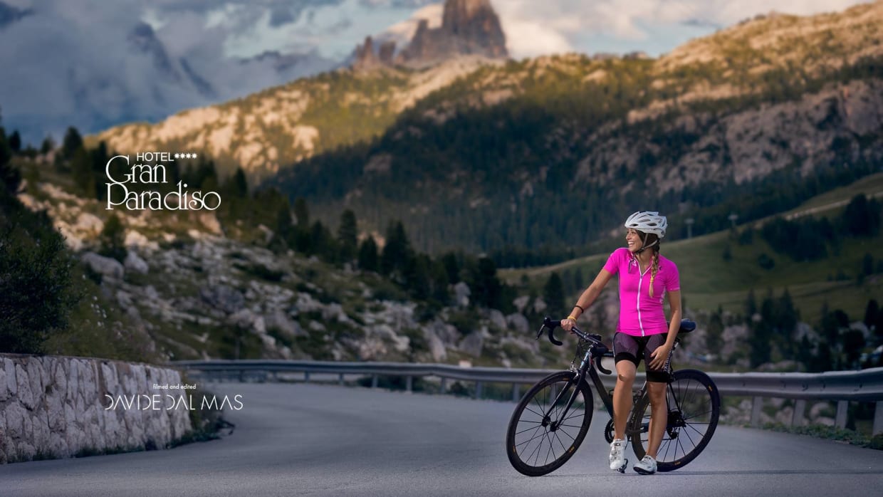 Frau mit Fahrrad auf Bergstraße vor Berglandschaft bei Hotel Gran Paradiso