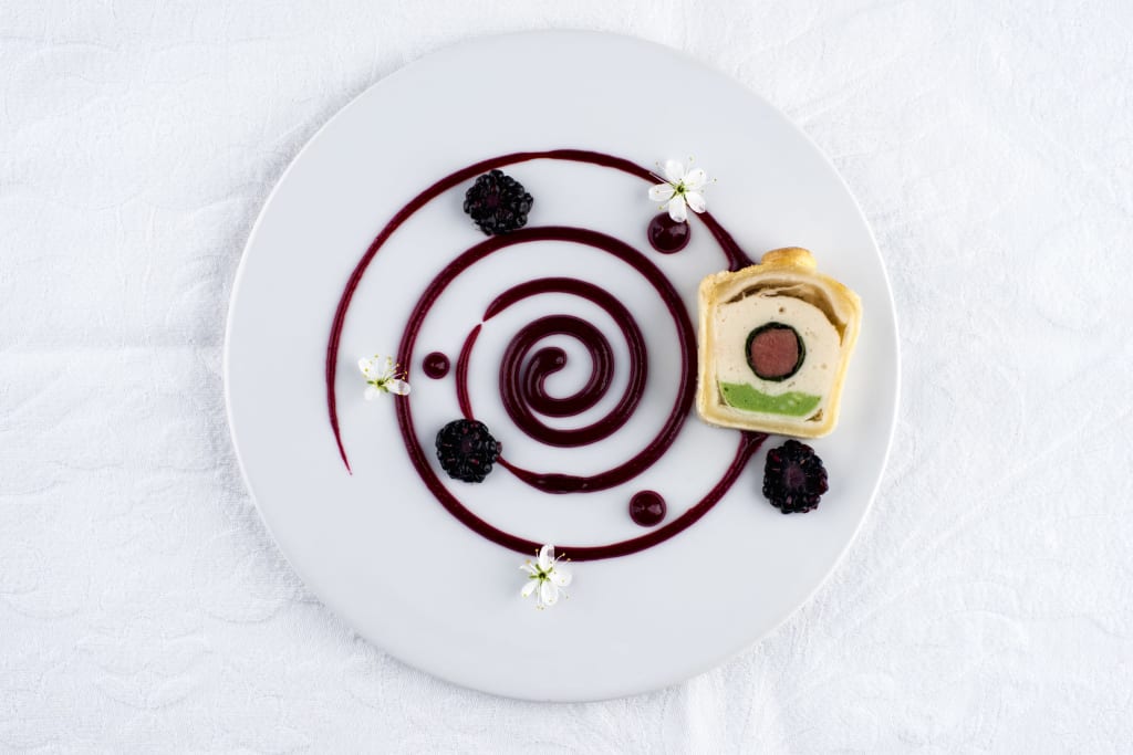 Kurz-Auszeit Kunstvoll angerichtetes Dessert mit Spiralsauce, Brombeeren und essbaren Blüten