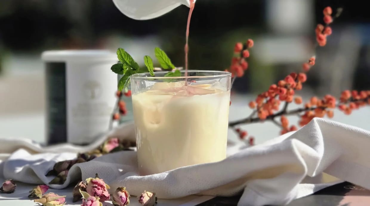Milchgetränk mit Eis und Minzblatt, mit rosa Flüssigkeit aufgegossen