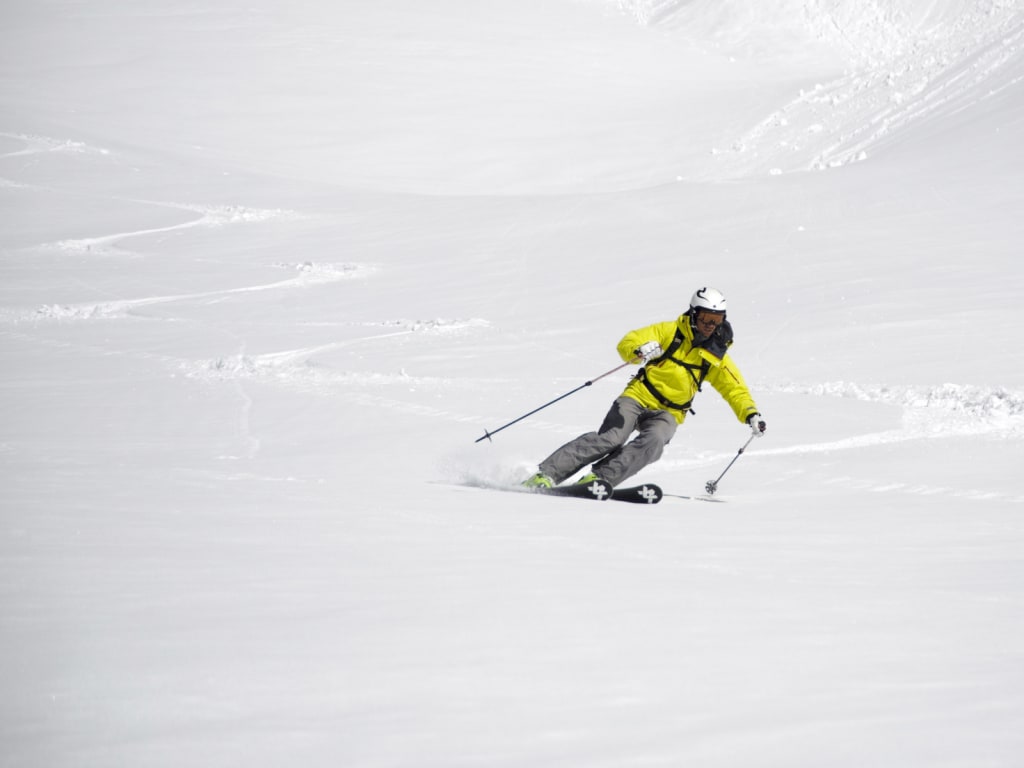 Skier in yellow jacket skiing down on fresh snow