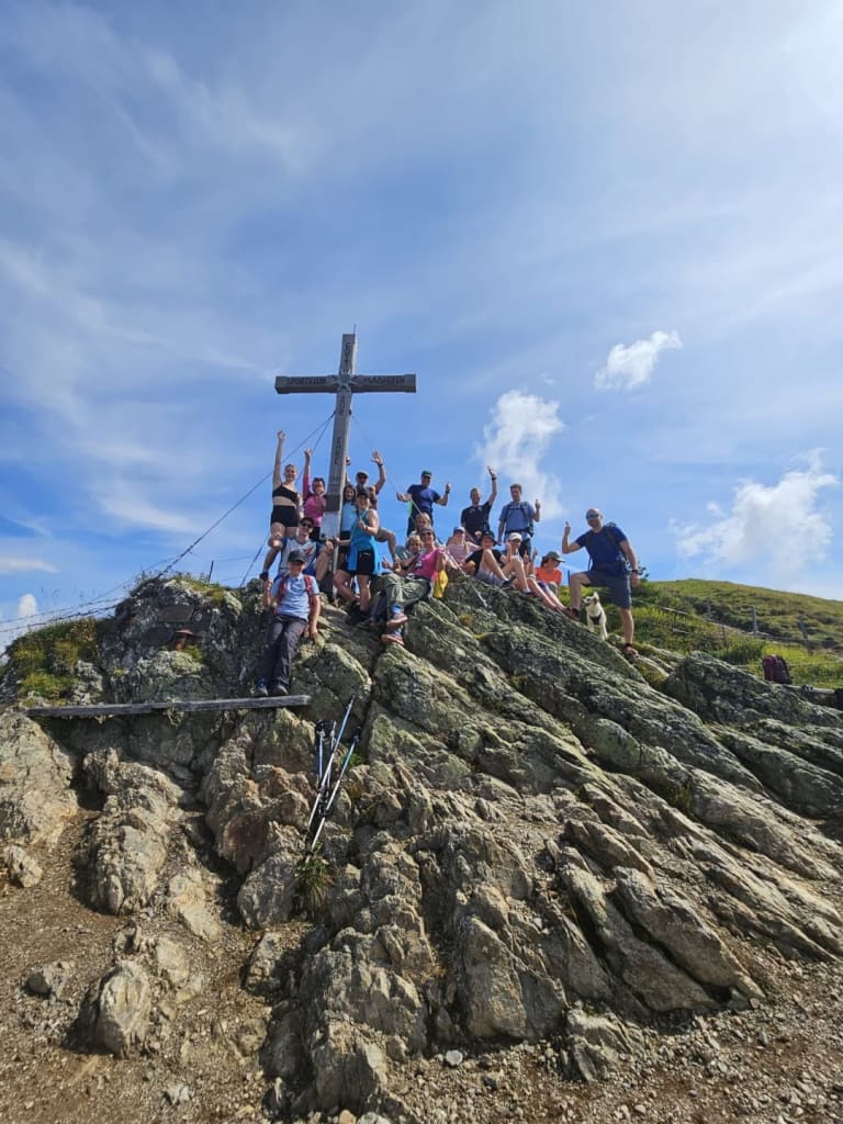 Group of hikers on rocky summit with large wooden cross on a sunny day