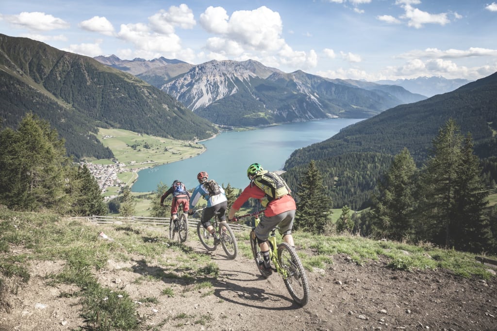 Tre mountain biker su un sentiero con vista sul lago e sulle montagne