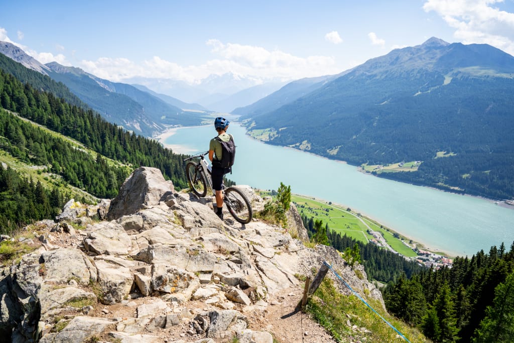 Cyclist on rocky mountain trail overlooking lake and mountains