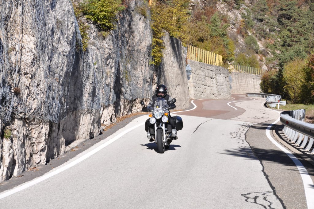 Motorcyclist riding on winding mountain road with rock face and safety net