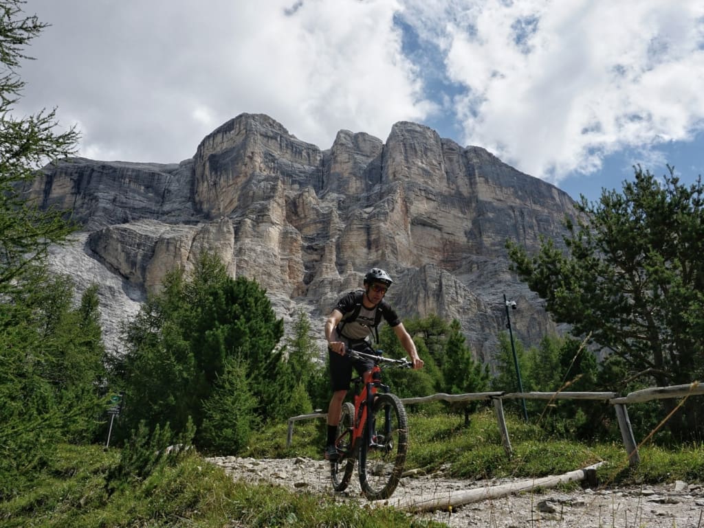 Mountainbiker fährt auf einem Waldweg vor hohen Felsen und bewölktem Himmel
