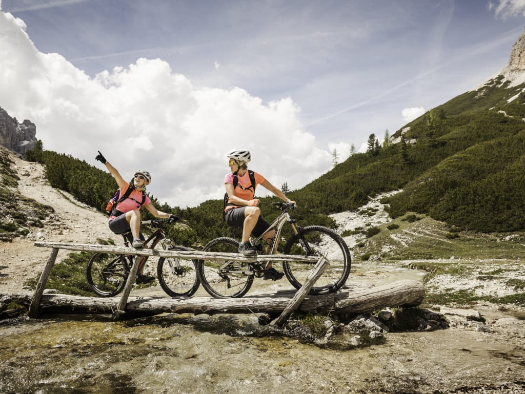 Two cyclists on a wooden bridge in mountainous terrain