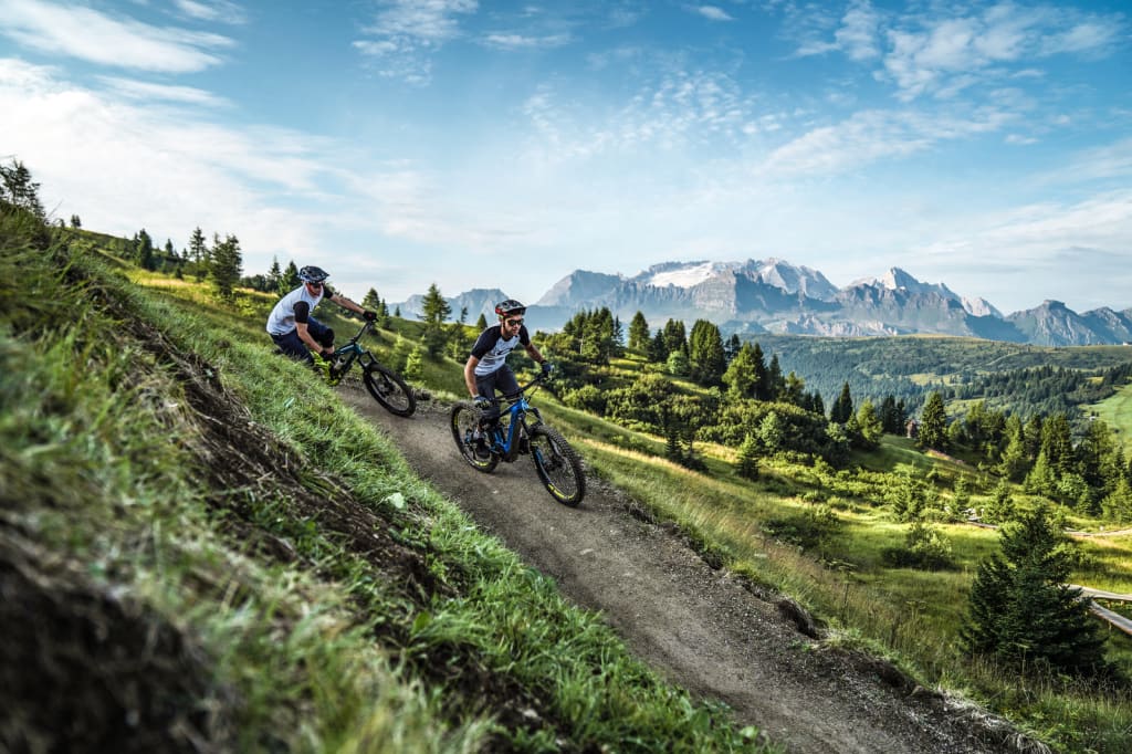 Two mountain bikers riding on a trail in the mountains with clear sky