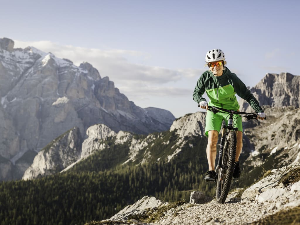 Donna in mountain bike su sentiero roccioso con montagne e foresta sullo sfondo