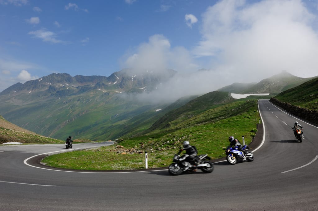 Motociclisti su strada di montagna tortuosa sotto cielo nuvoloso