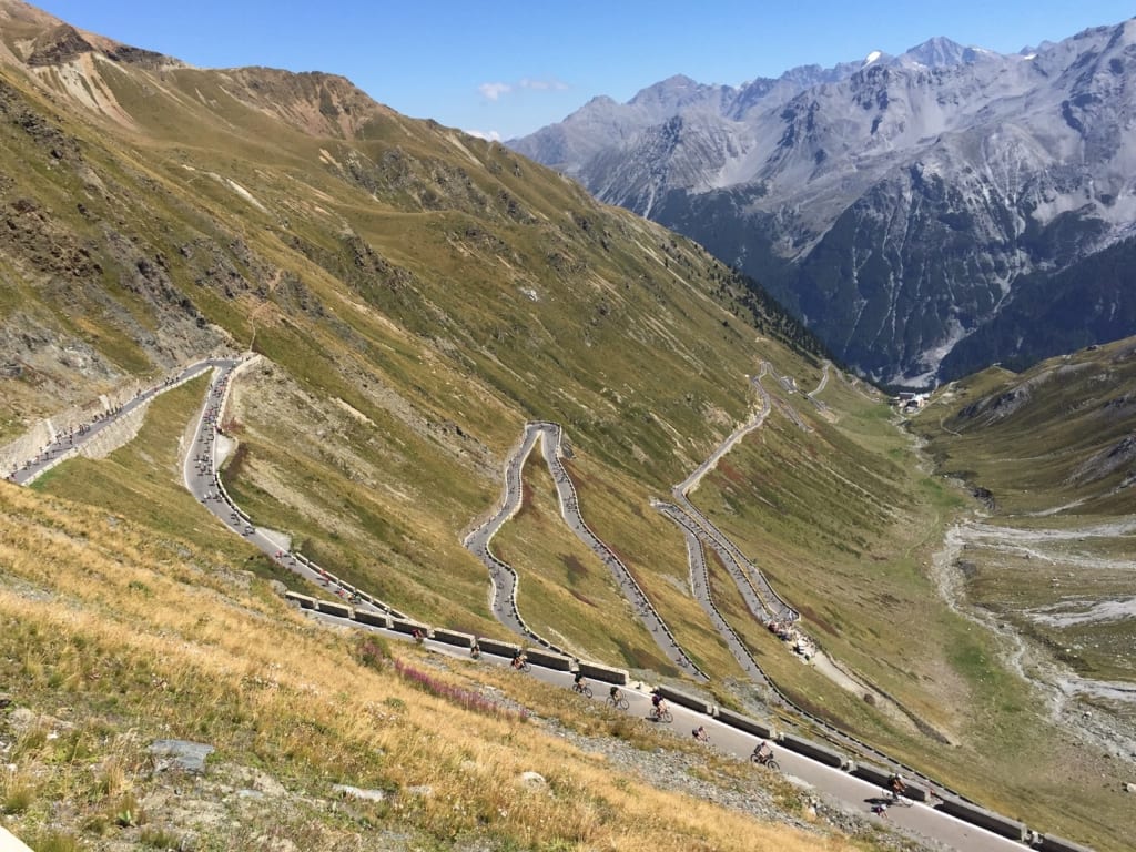 Mountain switchback road with cyclists and snow-capped peaks in the background