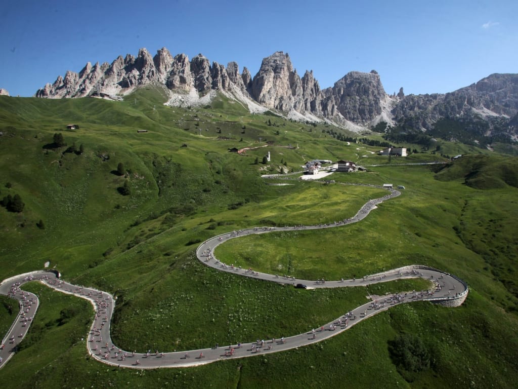 Winding mountain road with cyclists in green Alps under clear sky