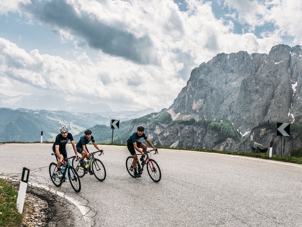 Three cyclists riding on a winding mountain road under cloudy skies