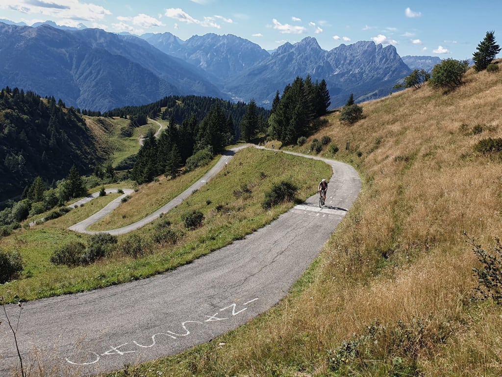 Cyclist riding on winding mountain road with Alps in background