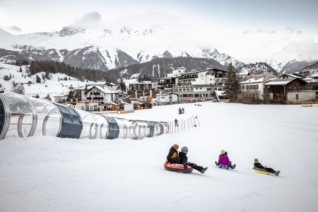 Kinderen sleeën van een besneeuwde helling bij een wintersportplaats met uitzicht op bergen