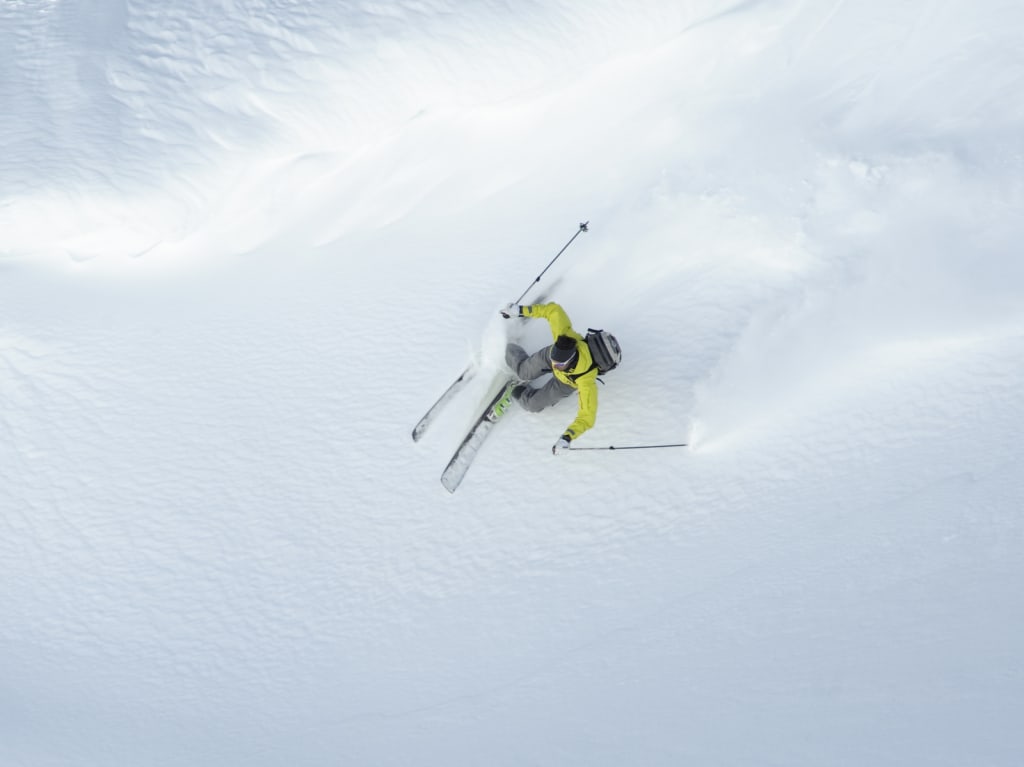 Sciatore con giacca gialla scia nella neve fresca