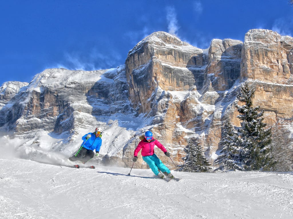 Dolomites Ski Week January Two skiers skiing on snowy slope with rocky mountains in background